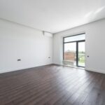 Bright and spacious modern room with a dark wooden floor and large window offering outdoor view.